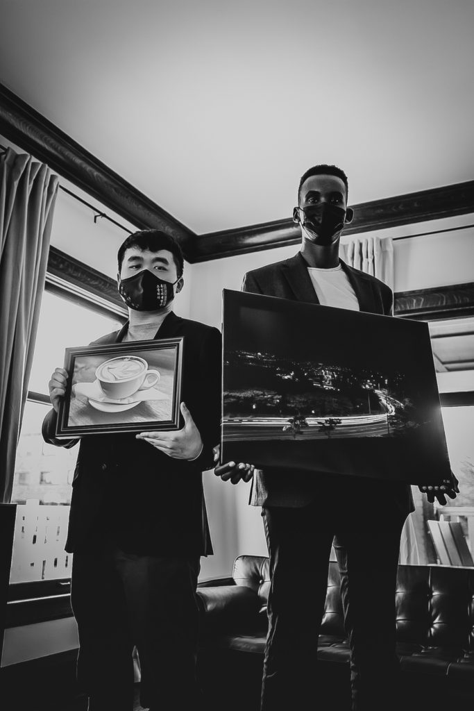 Sungmin "Steven" Suh and Kenneth Munyuza with 2 of Kenneth's photos that are on display at the Keppel House.  Steven and Kenneth are standing in the living room of the Keppel House holding two canvas photos. @createhopephotography