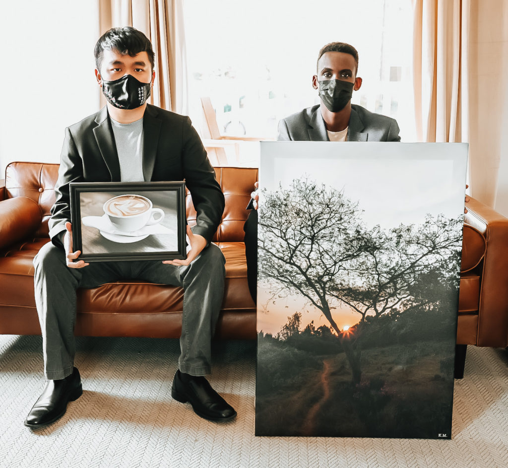 Sungmin "Steven" Suh and Kenneth Munyuza with 2 of Kenneth's photos that are on display at the Keppel House.  Steven and Kenneth are sitting on a couch in the living room of the Keppel House holding two canvas photos. @createhopephotography