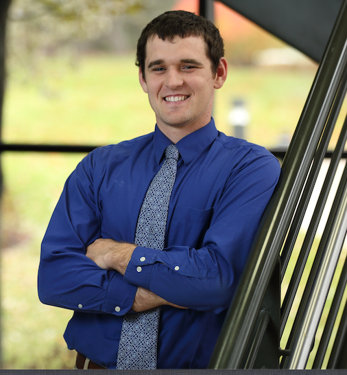 Alum Shawn Bates leans, smiling against a stair railing in professional attire.