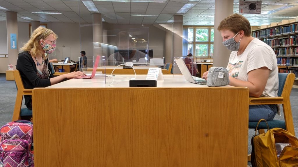 Two students sitting at a table in the library and maintaining a distance of six feet