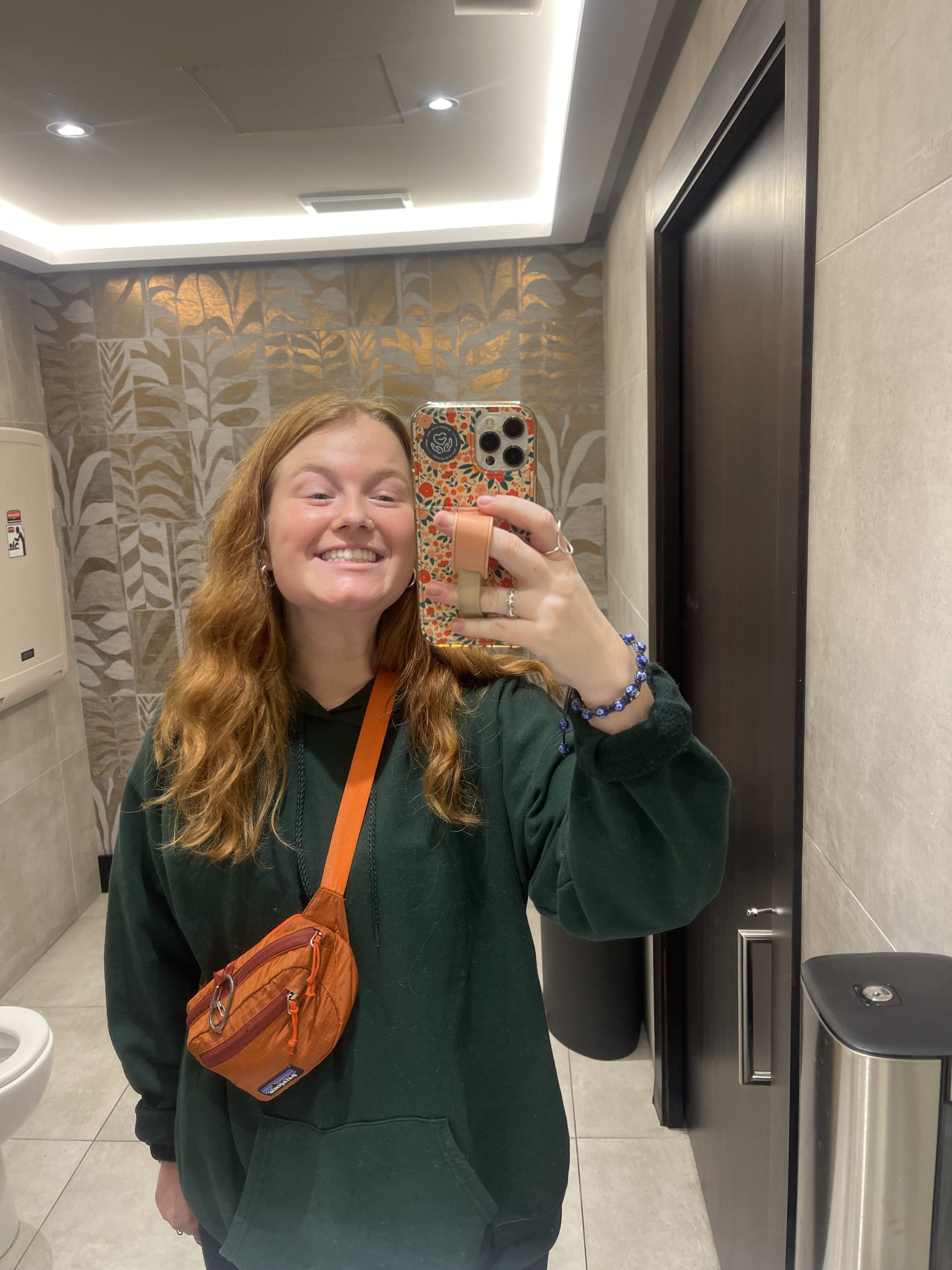 A mirror selfie in the bathroom mirror of a public restroom.