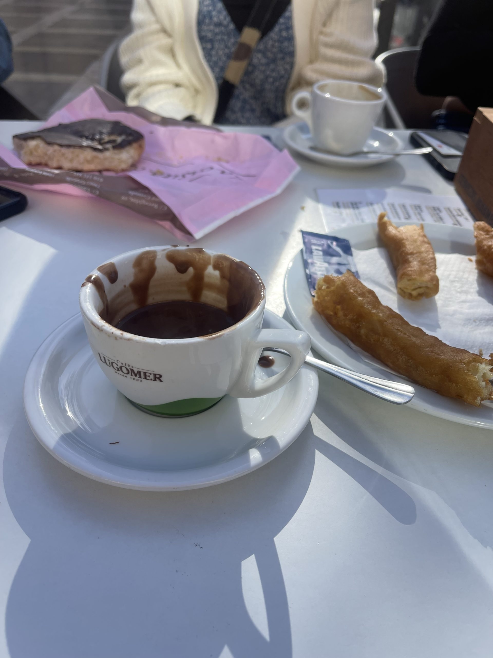 A picture of a mug of hot chocolate and a plate of churros on a table.