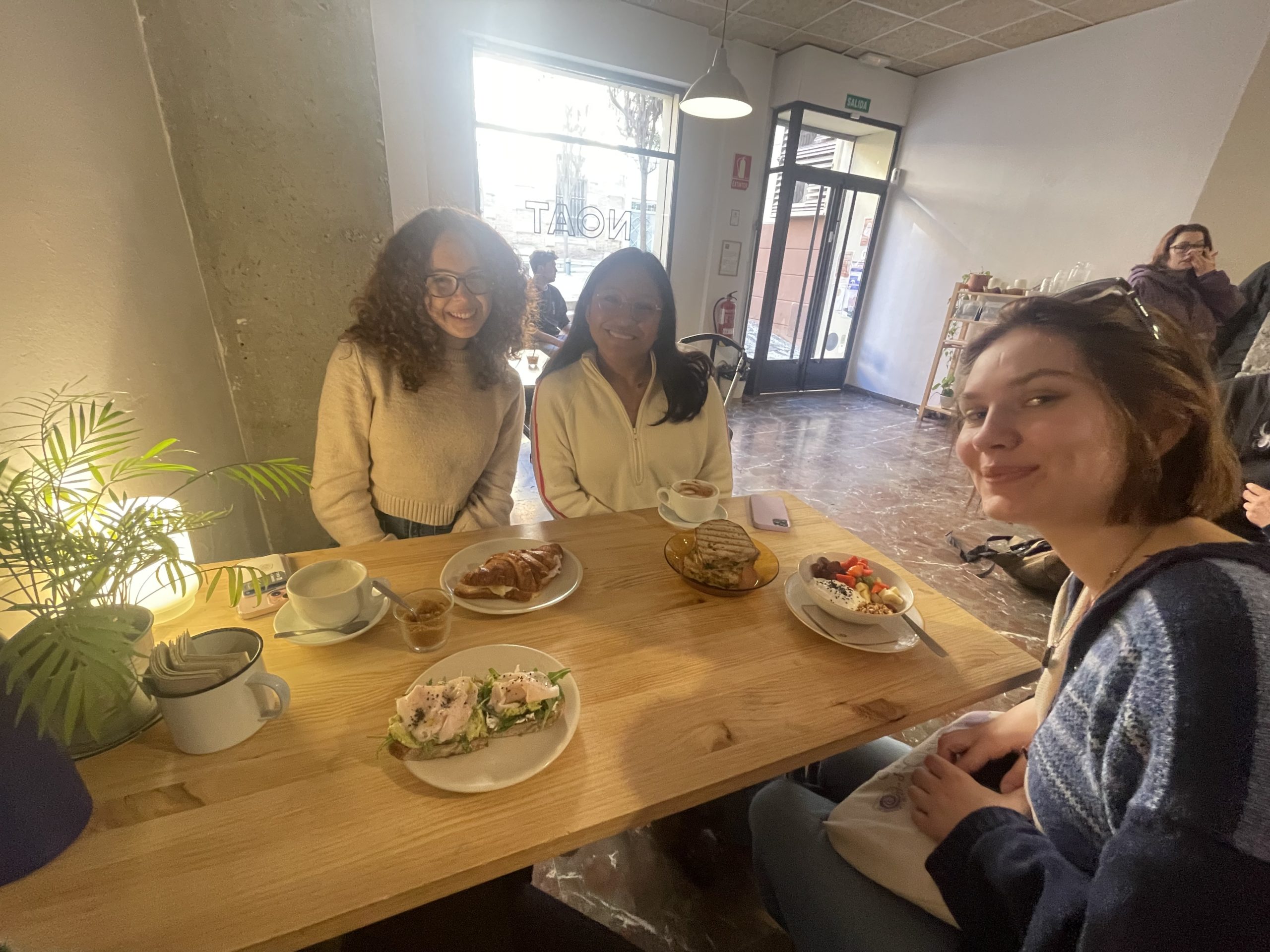 A table with four plates of food and three girls smiling.