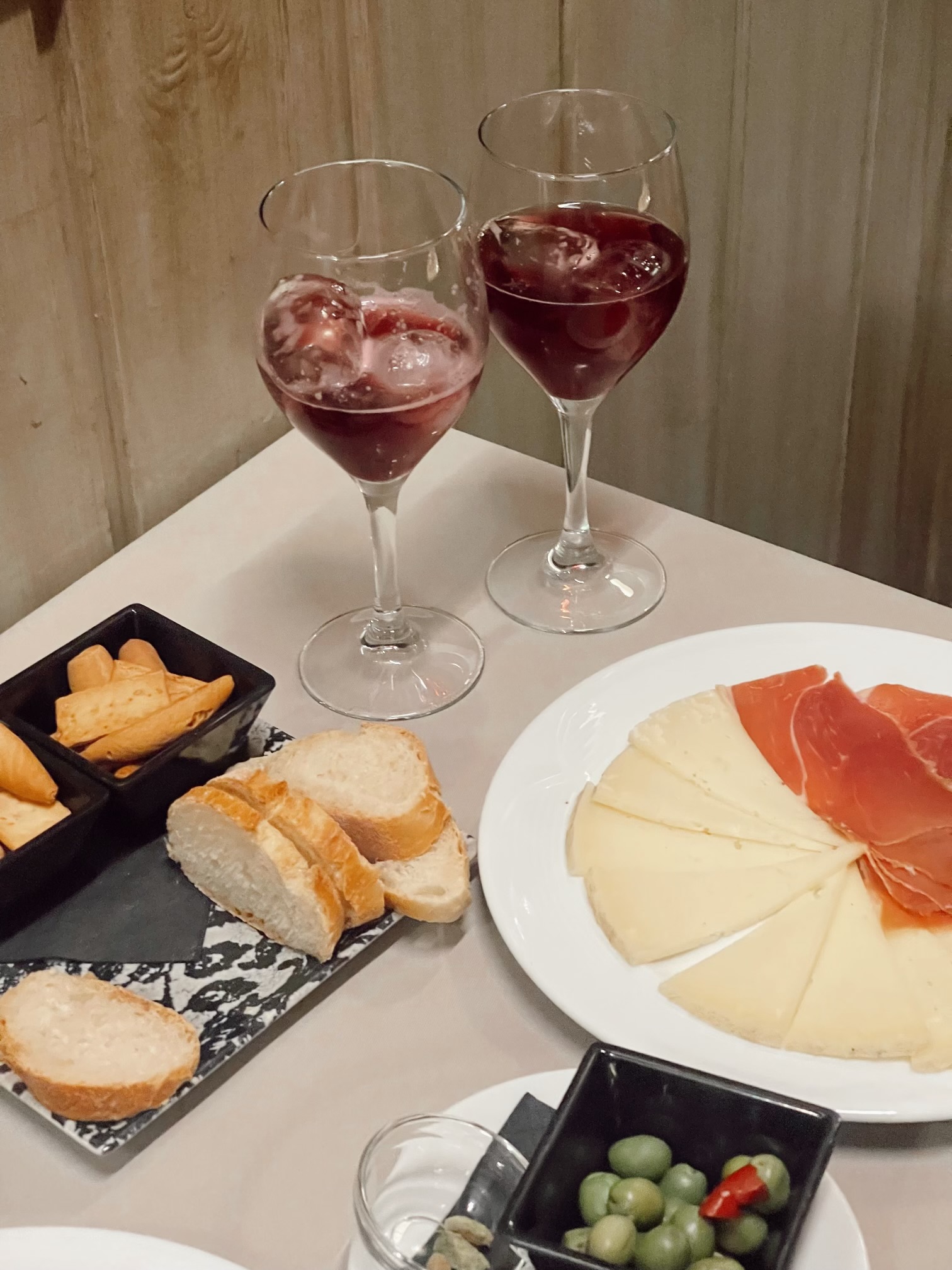 A picture of a table with cheese, ham, bread, and wine glasses on it.