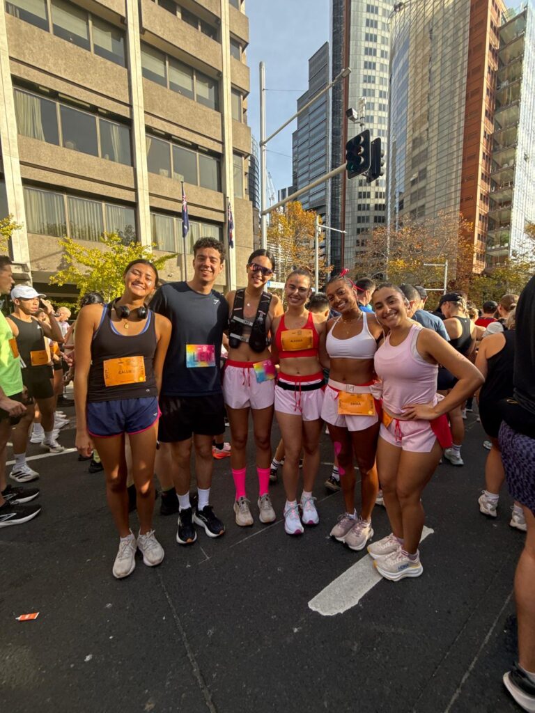 A group of friends posing together in downtown Sydney before or after the race, dressed in running gear and smiling in the middle of the city streets surrounded by other participants.