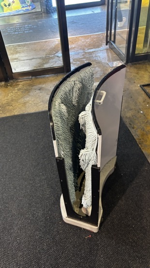 A freestanding umbrella dryer placed by the mall entrance, allowing shoppers to insert wet umbrellas to remove excess water before entering.