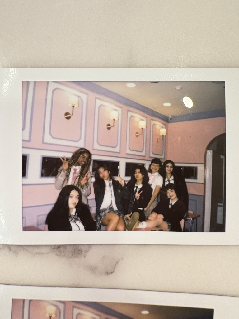 A photograph of seven people posing together in a pink-themed room
