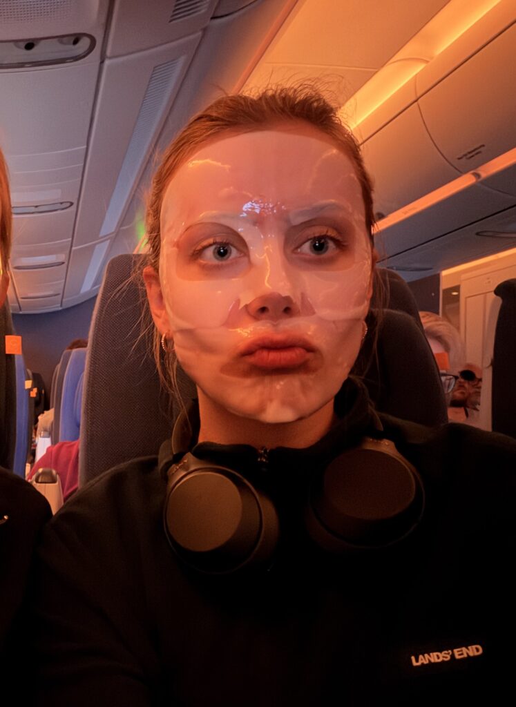 Close-up selfie with face mask,  face lit by vivid-orange lights; headphones rest around her neck. 