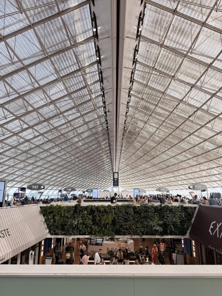 Glass and steel-roof, with shops and green planter-lined balcony inside of the airport in Paris. 