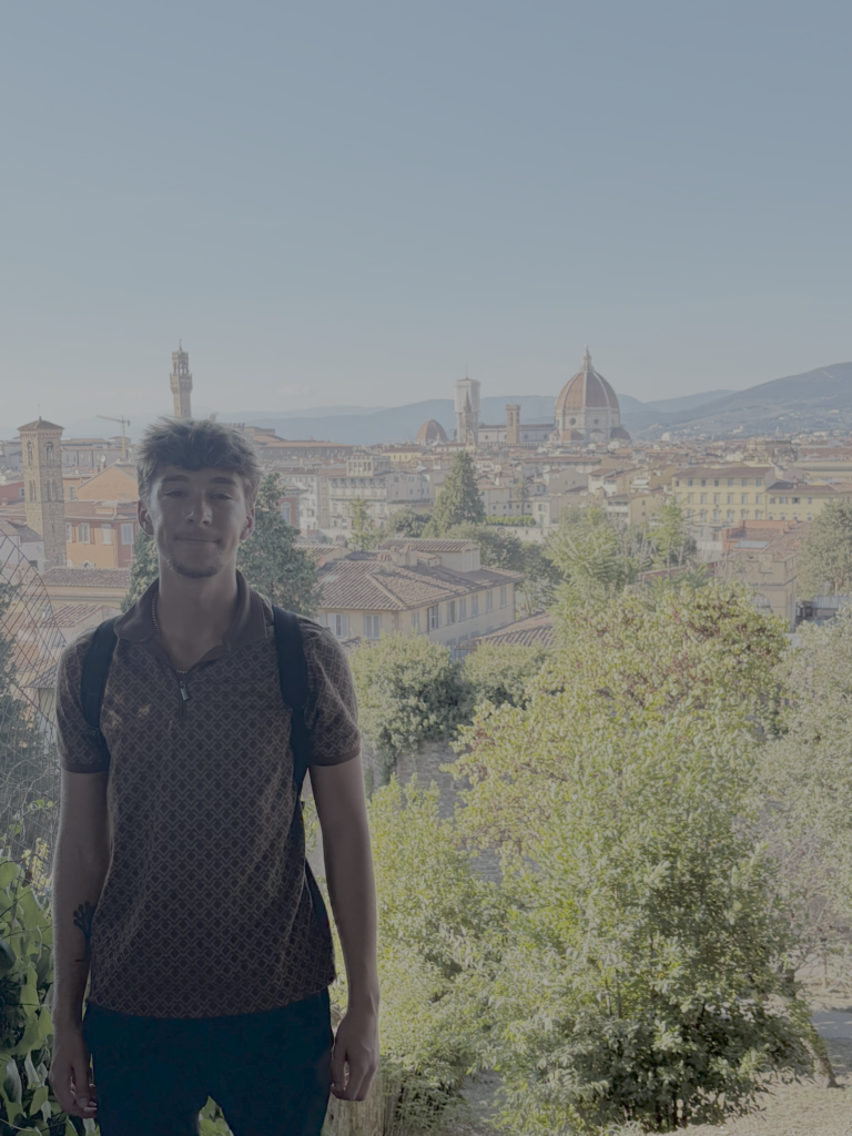 Young man (author this blog post) standing on a hill in Florence, Tuscany, with the old city center of Florence, including the Duomo, behind him in the distance on a sunny day.