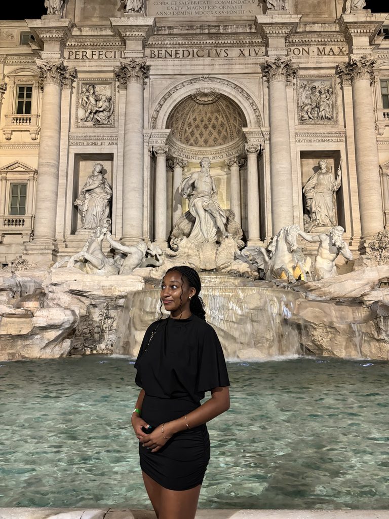 A photograph of a young woman (the author of the blog post) posing at night in front of the Trevi Fountain in Rome, Italy.