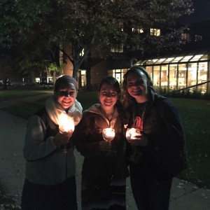 Three girls holding glasses with candles in them. 