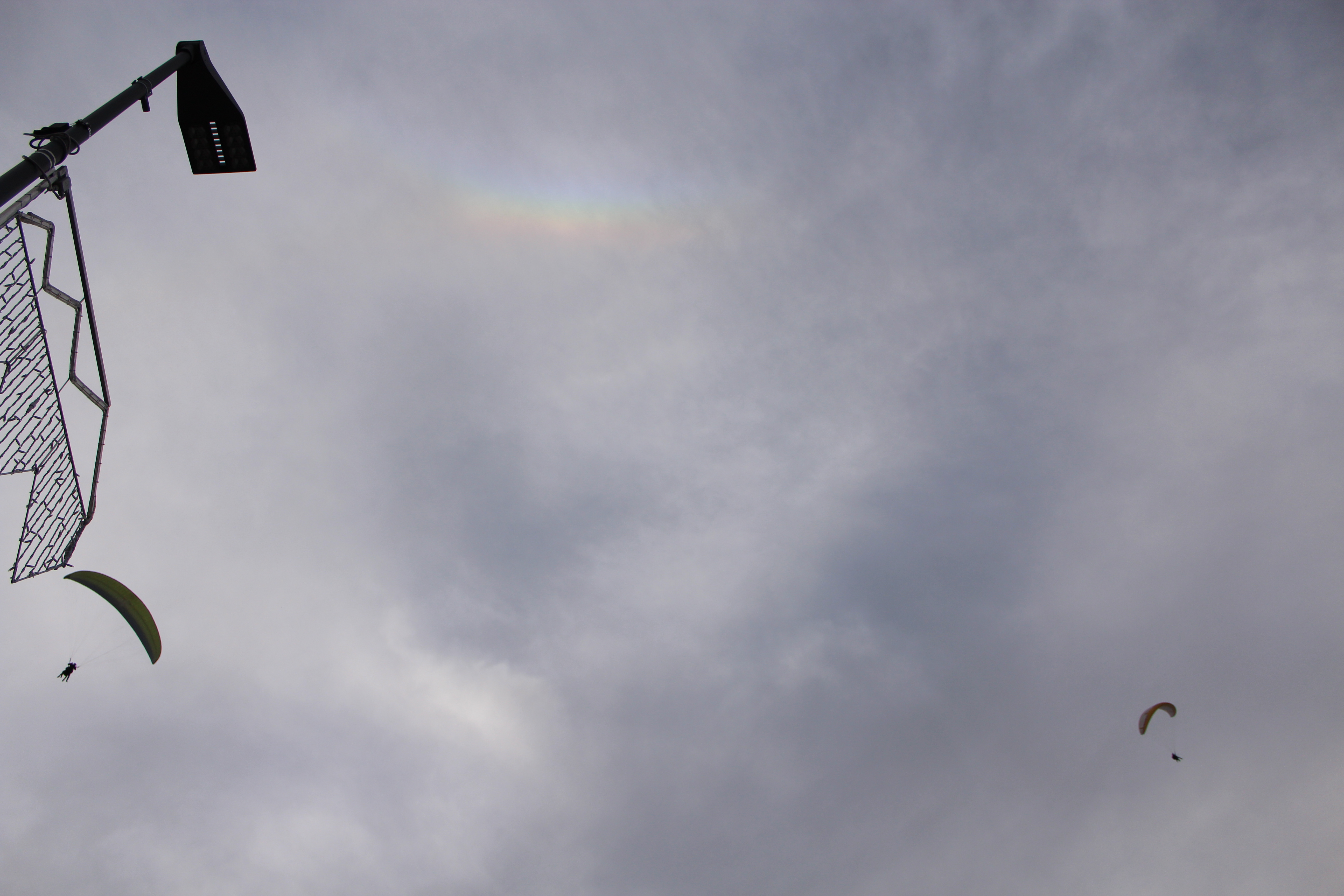 Paragliders and a patch of rainbow in the clouds